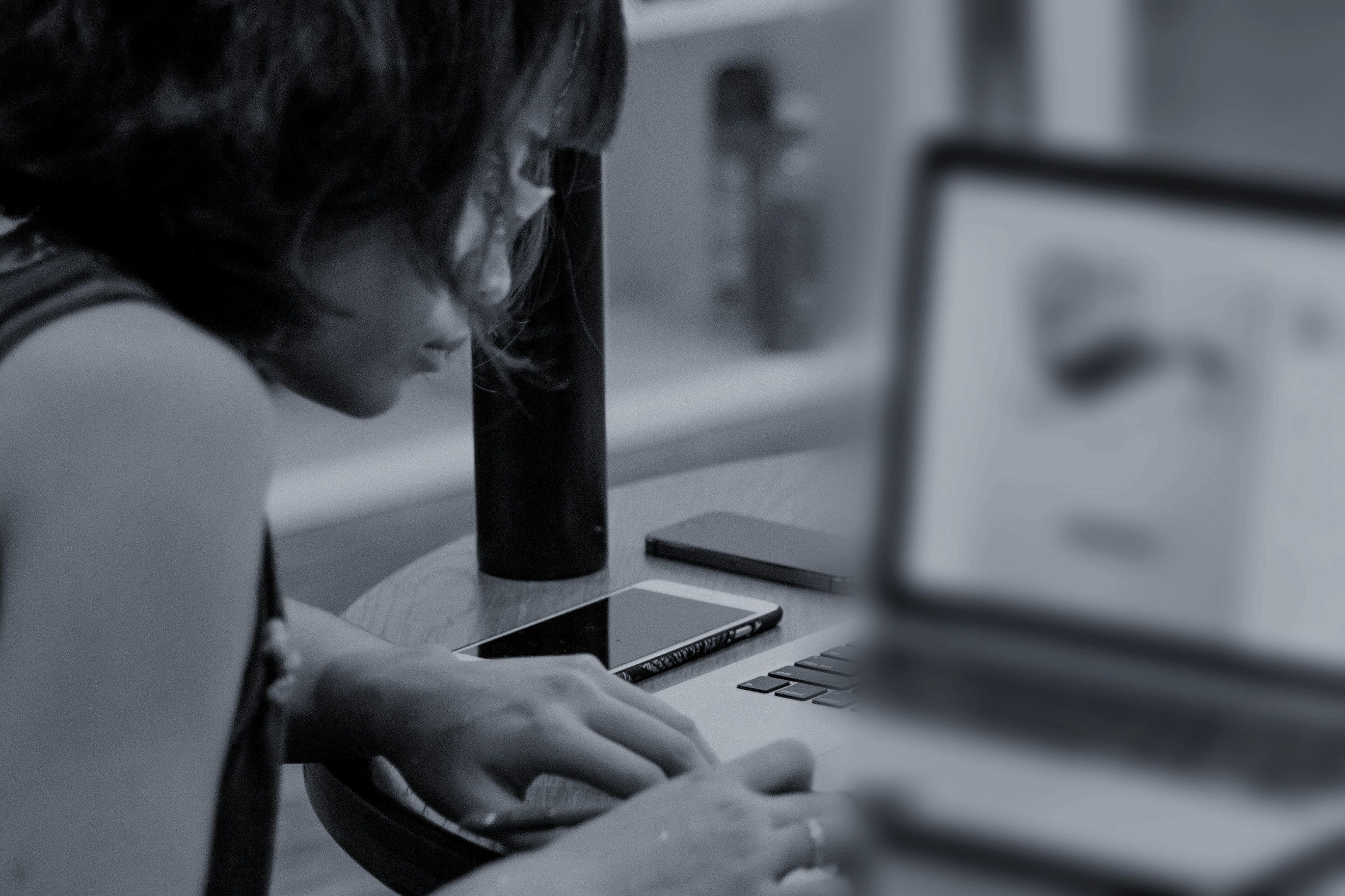 Eine Person sitzt halb abgewandt am Schreibtisch, die Hand am Trackpad, vor einem unscharfen Bildschirm